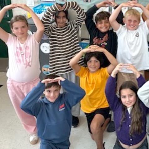 Reed students holding their arms above their heads to make the letter O.